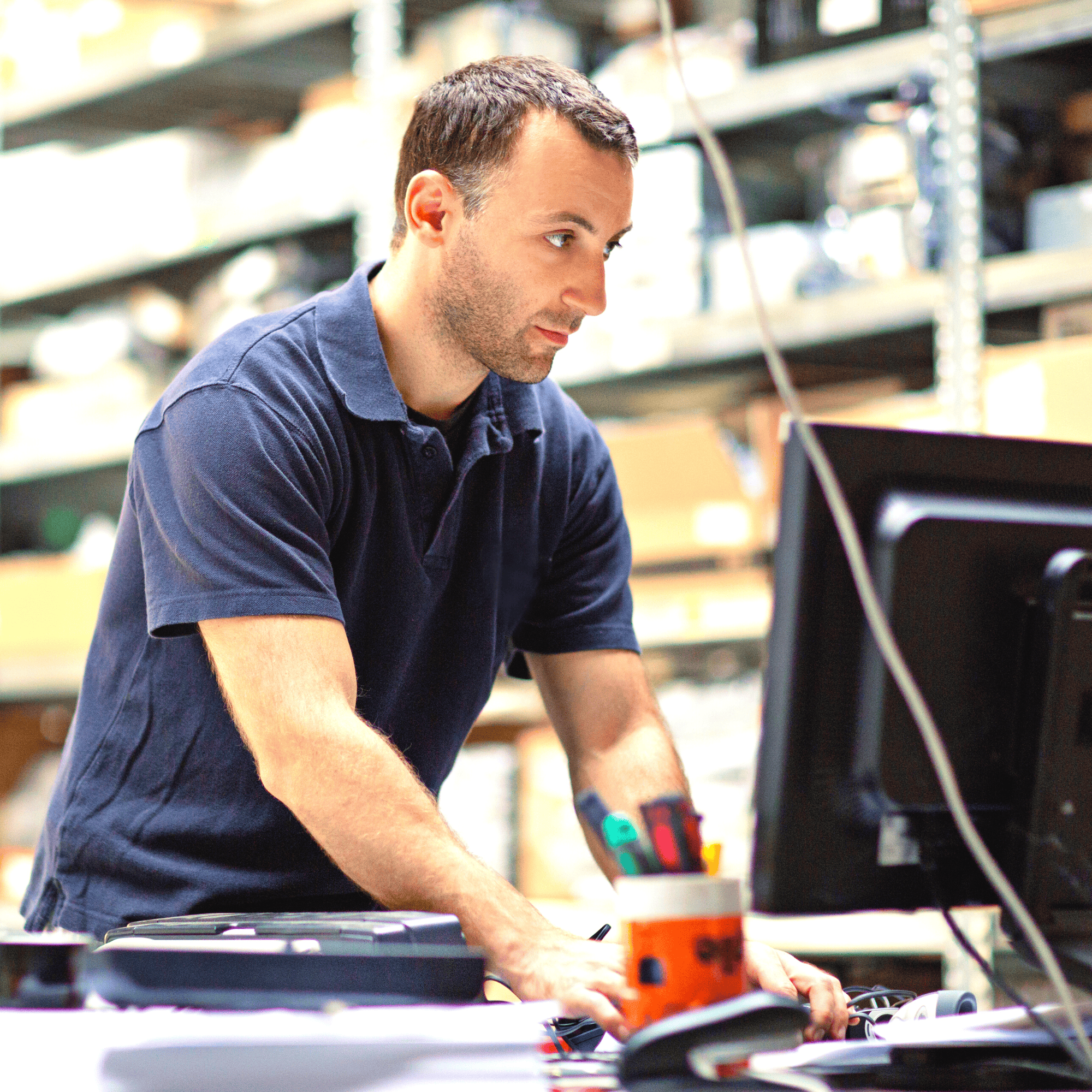 remote device | An operator is standing up a desk in a factory typing on a keyboard whilst he looks at a computer monitor